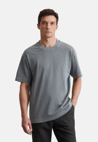 T-shirt en coton gris avec un col rond et des manches courtes, présentant une coupe décontractée et une texture lisse. Porté avec un pantalon sombre.