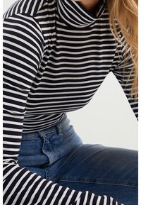 Marinblå och vit randig långärmad topp med hög krage; bärs med blå jeans. Har en smal passform och mjuk textur.