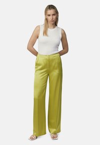 Szerokie satynowe spodnie w jaskrawym limonkowym kolorze, zestawione z dopasowanym białym topem z prążkowanej dzianiny. Spodnie mają gładką teksturę i dopasowany krój.