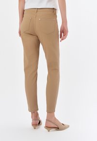 Beżowe, elastyczne spodnie o dopasowanym kroju, z dwoma tylnymi kieszeniami i gładką teksturą. Brzeg spodni jest lekko marszczony, co nadaje im zwężony wygląd.
