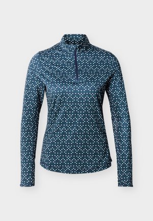 Sieviešu garām piedurknēm tumši zilā džemperī ar mazu baltu un zaļu ģeometrisku dimanta rakstu un ceturtdaļas rāvējslēdzēja augstu apkakli.