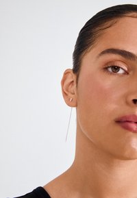 Hõbedased langetavad kõrvarõngad, millel on minimalistlik disain, väikese nõela ja pika, peene riputusahela kombinatsioon. Sile tekstuur ja tagasihoidlik sära.