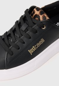 Adidași negri din piele cu guler cu imprimeu de leopard, șireturi negre, talpă albă și logo-ul auriu "Just Cavalli" pe lateral.