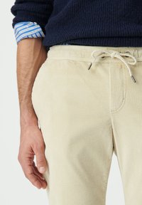 Pantalones de pana beige con una superficie texturizada, que cuentan con una cintura elástica con cordón y bolsillos laterales.