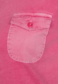 Tessuto di camicia rosa con una sola tasca sul petto dotata di bottone, texture liscia e un leggero gradiente di colore.