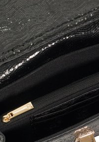 Black textured handbag interior with glossy finish, featuring a gold zipper and multiple pockets. Fabric material is smooth and durable.