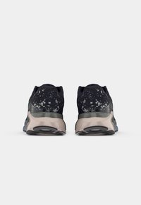 Zapatillas deportivas negras con parte superior moteada, entresuela gris en contraste y suela de goma texturizada. La vista trasera destaca el collar acolchado.