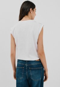 Hvid crop top med korte ærmer, parret med mørkeblå jeans i denim med baglommer og diskrete stikninger.
