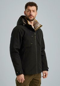 Zwarte capuchonjas met een rits aan de voorkant, een met bont gevoerde kraag en contrasterende gele accenten. Beschikt over twee voorzakken en knopenmanchetten.