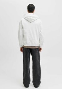 Lichtgrijze hoodie met een trekkoord, ribgebreide manchetten en zoom, gecombineerd met zwarte wijde jeans. Eenvoudig ontwerp, zachte textuur en neutrale kleuren.