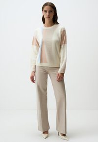 Maglione crema con blocchi di colore pastello, colletto e maniche a coste. Abbinato a pantaloni beige e décolletées bianche a punta. Texture liscia.