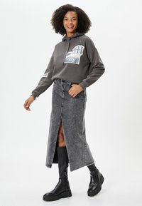 Grijze hoodie met een graphic, gecombineerd met een lange grijze spijkerrok met een split aan de voorkant en zwarte chunky laarzen.