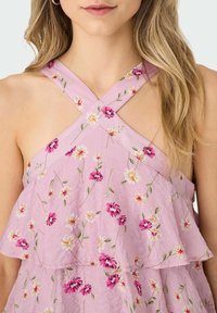 Lila virágmintás ruha keresztben futó pántokkal, réteges fodrokkal és rózsaszín és sárga hímzett virágokkal egy textúrált anyagon.