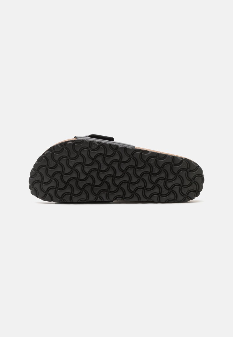 Schwarze Gummisohle mit einem wellenförmigen Muster, die eine korkähnliche Fußbett und einen verstellbaren Riemen zeigt. Minimalistisches Design und flaches Profil.