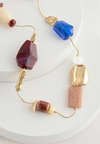 Collier en perles avec des pierres texturées rouges, bleues et crème ; accents dorés ; diverses formes, y compris rectangulaires et ovales.