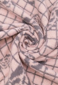 Sciarpa lavorata a maglia di un delicato rosa, con una texture morbida, caratterizzata da un motivo geometrico grigio e una piega a spirale per l'esposizione.