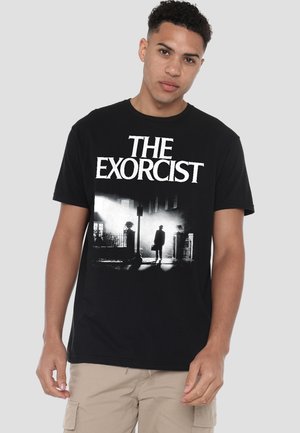Young man wearing a black "The Exorcist" t-shirt featuring a silhouette of a man standing in a foggy street scene.
