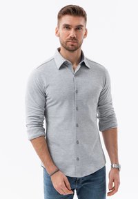 Grijze langwerpige blouse met een button-down kraag, met een zachte katoenmix textuur en opgerolde mouwen, gecombineerd met blauwe spijkerbroeken.