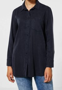 Tmavě námořnická košile s dlouhým rukávem vyrobená z hladké tkaniny, s knoflíkovým zapínáním, límečkem a kapsou na levé straně hrudi. Nosit s modrými džínami.