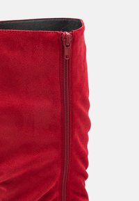Botín de ante rojo hasta el tobillo con cremallera lateral, textura suave y detalle de diseño gathered a lo largo del eje.
