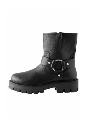 Black leather ankle boot with textured surface, rounded toe, and a decorative buckle strap. Thick, rugged sole with grooved pattern.