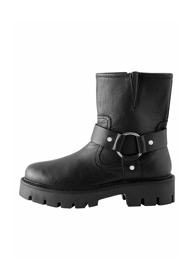 Black leather ankle boot with textured surface, rounded toe, and a decorative buckle strap. Thick, rugged sole with grooved pattern.