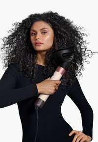 Haarföhn met een zwarte mondstuk en een lichtroze handvat met een gestructureerde grip; model gekleed in een zwart geribbeld topje.