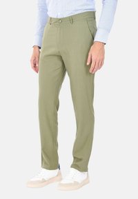 Pantaloni da uomo verde oliva realizzati in tessuto leggero, con una vestibilità slim, due tasche, chiusura con bottone e indossati con sneakers bianche.