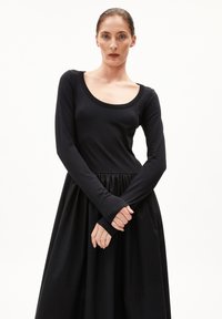 Das schwarze langärmlige Kleid zeichnet sich durch einen taillierten Oberteil mit einem runden Ausschnitt und einem gathered, voluminösen Rock aus, der aus weichem, fließendem Stoff gefertigt ist.