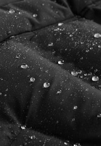 Tela negra acolchada con un acabado resistente al agua; presenta pequeñas gotas de agua y un patrón acolchado con costuras visibles.