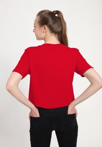 Rød kortærmet T-shirt lavet af glat stof, med rund hals og en afslappet pasform, parret med sorte stramme jeans.
