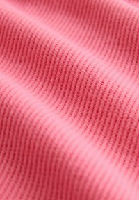 Textúrovaná tkanina v jemnej ružovej farbe, zdobená vertikálnymi rebrovanými vzormi. Materiál pôsobí teplo a ľahko, s hladkým povrchom.