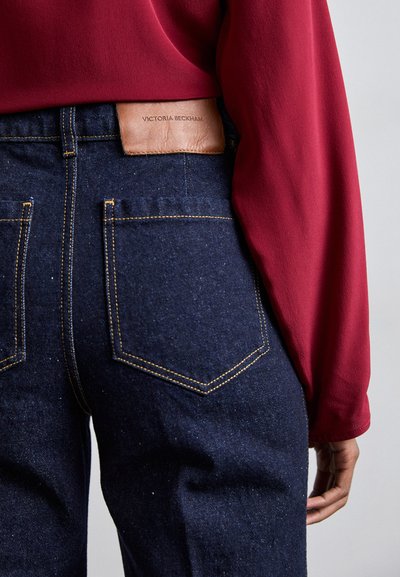 Τζιν παντελόνι με σκούρο μπλε απόχρωση, με πορτοκαλί ραφές, δύο πίσω τσέπες �και δερμάτινη ετικέτα σε μπεζ χρώμα με την επιγραφή "Victoria Beckham".
