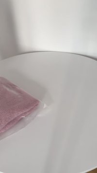 Pink knitted fabric in transparent packaging, laid on a smooth white surface, displaying soft texture and folded edges.