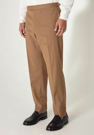Brown tailored trousers with a smooth texture, featuring a side adjuster, and paired with black leather loafers.
