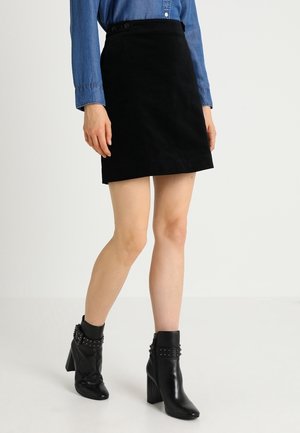Frau trägt einen schwarzen Minirock, ein blaues langärmliges Hemd mit Knöpfen und schwarze hochhackige Stiefeletten mit genieteten Riemen.