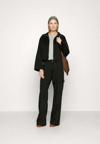 Black cropped jacket, gray t-shirt, and black cargo pants. Brown handbag and brown shoes. Smooth fabric with a relaxed fit and wide legs.
