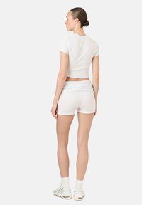 Biely priliehavý crop top a zodpovedajúce šortky vyrobené zo strečového materiálu. Top má krátke rukávy a šortky sa vyznačujú prehnutým pásom.