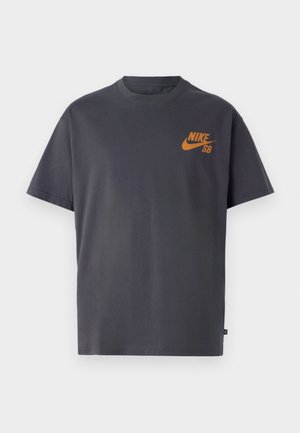 T-shirt gris à manches courtes en coton. Présente un logo Nike SB orange sur la poitrine gauche. Conception à col rond avec une coupe décontractée.