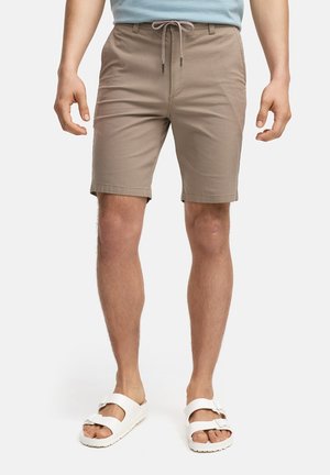 Shorts en coton beige avec une taille élastique et un cordon de serrage. Présente des poches avant et une coupe droite, associés à des sandales blanches.