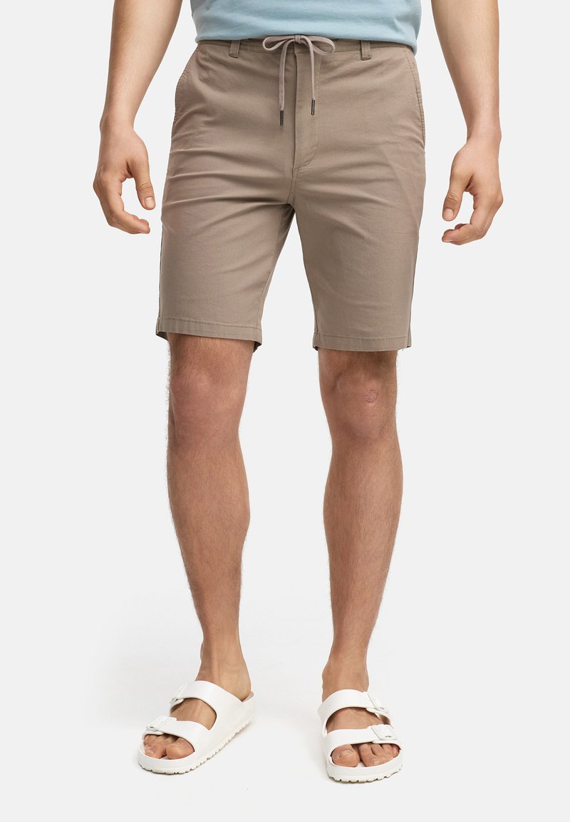 Beige bomullshorts med elastisk midje og snorstengning. Har frontlommer og rett passform, kombinert med hvite sandaler.