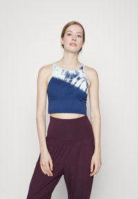 Top cropped azul-marinho feito de um tecido suave com um padrão tie-dye em branco na gola, combinado com calças roxas de cintura alta.