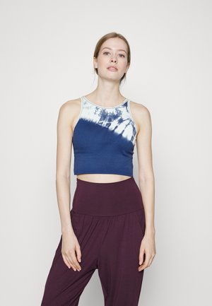 Top cropped azul-marinho feito de um tecido suave com um padrão tie-dye em branco na gola, combinado com calças roxas de cintura alta.
