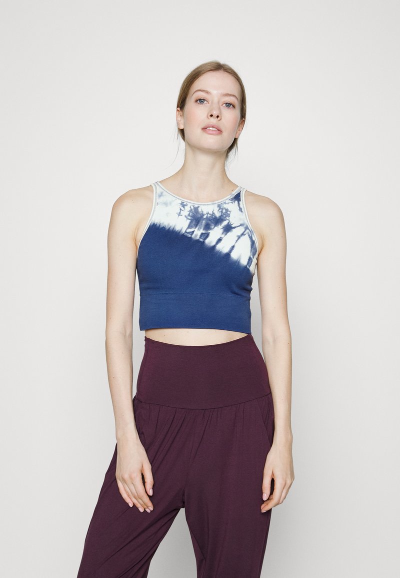 Top cropped azul-marinho feito de um tecido suave com um padrão tie-dye em branco na gola, combinado com calças roxas de cintura alta.