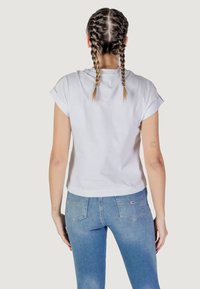 T-shirt bianco in cotone con maniche arrotolate, vestibilità rilassata e orlo dritto, abbinato a jeans in denim blu a vita media. Nessun dettaglio notevole.