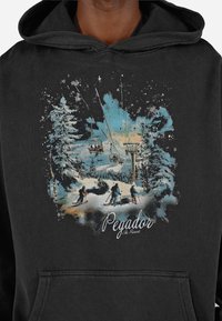 Μαύρο φούτερ με κουκούλα που απεικονίζει μια πολύχρωμη χειμερινή σκηνή με χιόνι, δέντρα, σκιέρ και αναβατήρα σκι, με την ένδειξη "Θέρετρο Σκι Pegador."