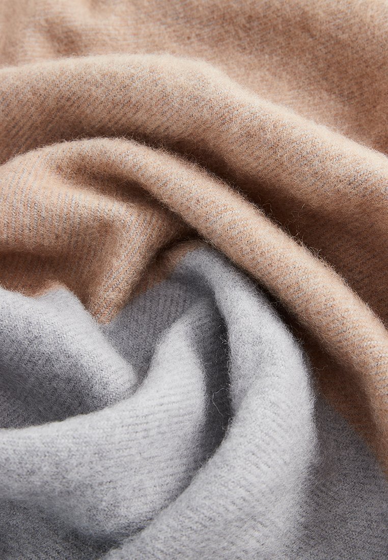 Weiches, gefaltetes Gewebe in Beige- und Hellgrautönen, das Textur und sanfte Kurven zeigt und ein gemütliches, wolliges Aussehen hat.