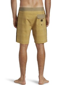 Maillots de bain à carreaux jaunes avec une taille solide beige, une poche arrière et des détails sur les côtés. Le tissu semble lisse avec un design léger.