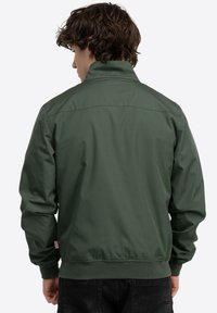 Chaqueta bomber verde con un cuello alto y puños elásticos, que presenta una textura suave y un diseño minimalista. Sin logotipos ni patrones visibles.