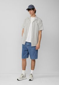 Gestreepte kortekorte overhemd met knopen in wit en blauw, gecombineerd met blauwe denimshorts. Draagt grijze sneakers met witte accenten en sokken.